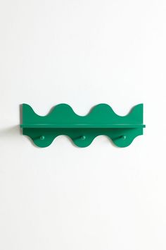 a green wall mounted shelf on the side of a white wall with two hooks attached to it