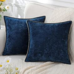 two blue pillows sitting on top of a white couch next to a vase with flowers