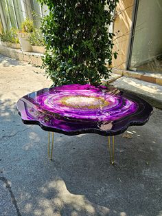 a purple glass table sitting on top of a sidewalk next to a tree and building