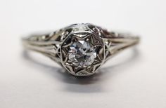 an old - fashioned diamond ring with filigrees sits on a white surface