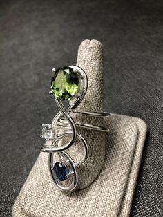 I've created this Bohemian abstract large finger ring, a true statement piece, in sterling silver, which features a 10x8mm oval Peridot, a 6mm White Topaz and an 8x6mm Blue Zircon. I make everything in 925 Sterling Silver and can Rhodium plate if you wish over the piece. I use AA+ grade gemstones in my work. The ring base is 12 gauge round sterling silver wire. No two are alike has I hand-fabricate one-of-a-kind designs. This statement ring is sturdy and I soldered many contact points and harden Modern Sterling Silver Crystal Gemstone Ring, Sterling Silver Freeform Rings As Gifts, Modern Crystal Gemstone Ring In Sterling Silver, Silver Peridot Rings In Fine Jewelry Style, Unique Multi-stone Sterling Silver Rings, Silver Peridot Rings Fine Jewelry, Modern Sterling Silver Jewelry With Accent Stones, Unique Silver Topaz Sterling Silver Ring, Fine Jewelry Sterling Silver Bypass Ring