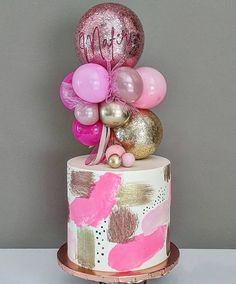 a pink and gold birthday cake with balloons