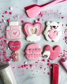 decorated cookies with pink icing on a white table next to utensils and spoons