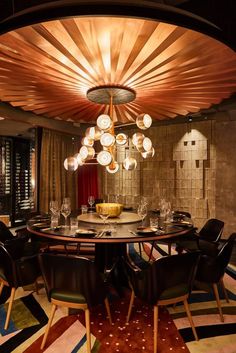 a dining room with a round table surrounded by black leather chairs and gold chandelier