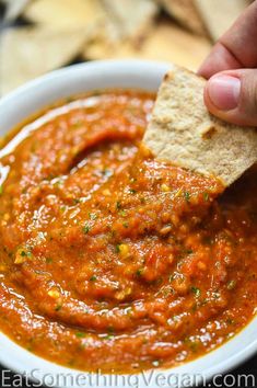 a hand dipping a tortilla chip into a bowl of salsa