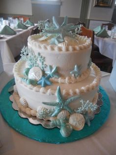 a three tiered cake decorated with seashells and starfish on a table