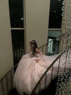 a woman in a pink ball gown sitting on the stairs at a staircase case with beads hanging from it