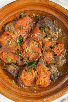 a wooden bowl filled with meat and vegetables on top of a white table next to utensils