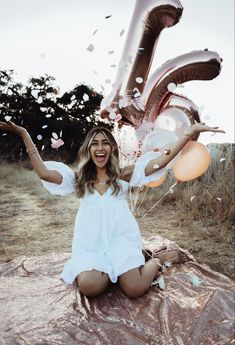 a woman is sitting on the ground with balloons and confetti in her hands