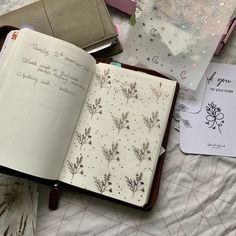 an open notebook sitting on top of a bed next to a notepad and pen