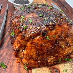 a large piece of meat sitting on top of a wooden cutting board next to a knife and fork