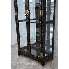 a black china cabinet with gold trimmings on the glass doors and two shelves