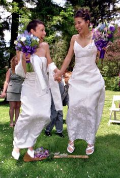 two brides holding hands and walking in the grass with purple flowers on their feet