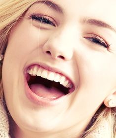 a close up of a person smiling and holding a cell phone to their ear