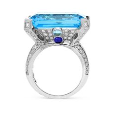 Bold and feminine, this gemstone ring defines a beautiful design showcasing an emerald cut blue topaz center stone in a diamond adrorned setting. On either side of the center gemstone lay two smaller round blue topaz and a cabochon cut blue sapphire for extra detailing. The ring flows into an embellished shank to enhance an eye catching appeal. Polished to a bright shine, this look packs a big visual punch. 
24.80 carat Emerald cut Blue topaz
0.60 carat cabochon round cut Sap Blue Radiant-cut Emerald Ring In Fine Jewelry Style, Blue Radiant Cut Emerald Ring In Fine Jewelry, Blue Asscher Cut Emerald Ring In Fine Jewelry Style, Blue Radiant-cut Emerald Ring Fine Jewelry, Blue Radiant Cut Emerald Ring Fine Jewelry, Luxury Blue Radiant Cut Diamond Ring, Luxury Blue Radiant Cut Ring, Blue Asscher Cut Emerald Ring, Fine Jewelry, Blue Diamond Emerald Ring In Fine Jewelry Style