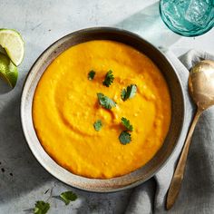 a bowl of carrot soup with cilantro and lime on the side next to a spoon