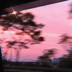 the sky is pink and purple as seen through a car window with trees in the foreground