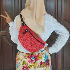 a woman wearing a hijab and carrying a red crochet purse on her back