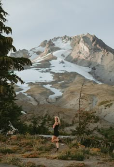 a woman standing on top of a mountain next to trees and snow covered mountains in the background