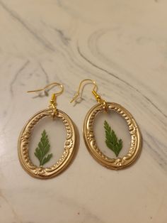 "These framed pressed flower earrings are handmade and use crystal clear hot glue to allow the flower to be seen inside the frame. The earring hooks are hypoallergenic, gold-plated stainless steel and come with a rubber back. The framed pressed flowers measure 1.25\"x1\" for the oval frame and 1\"x0.75\" for the rectangular frame. The flower color and frame shape can be customized." Gold Botanical Earrings With Pressed Flowers, Botanical Gold Earrings With Pressed Flowers, Botanical Gold Earrings With Birth Flower, Gold Resin Earrings With Birth Flower Detail, Gold Resin Earrings With Birth Flower, Nature-inspired Gold Earrings With Pressed Flowers, Nature-inspired Gold Flower Earrings With Pressed Flowers, Nature-inspired Gold Flower Earrings With Ear Wire, Handmade Gold Botanical Earrings