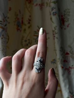 a woman's hand with a ring on it and a flowered curtain behind her