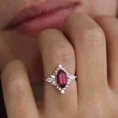 a close up of a person's hand wearing a ring with a red stone