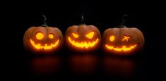 three jack o lantern pumpkins glowing in the dark with their faces carved into them