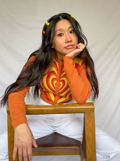 cropped orange cardigan with red, orange, and yellow heart design available in sizes xs, s, m, l model is 5'3" and wearing a size small Fitted Heart Print Sweater For Fall, Orange Fitted Long Sleeve Cardigan, Fitted Orange Long Sleeve Cardigan, Fitted Long Sleeve Orange Cardigan, Fitted Orange Cardigan For Spring, Retro Orange Spring Cardigan, Orange Fitted Trendy Sweater, Fitted Trendy Orange Sweater, Trendy Fitted Orange Sweater