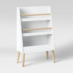 a white book shelf with wooden legs and two shelves on each side, in front of a gray background