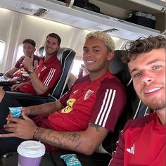 three men in red shirts sitting on an airplane