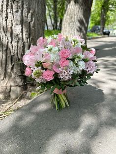 a bouquet of pink and white flowers sitting on the ground in front of a tree