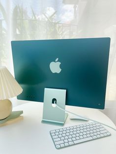 an apple computer sitting on top of a white desk next to a lamp and keyboard