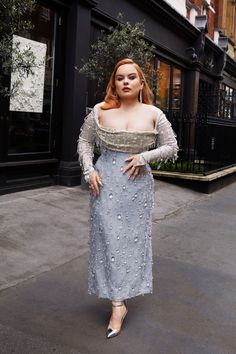 a woman is standing on the sidewalk wearing a dress with pearls and long sleeves in front of a building