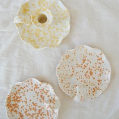 three pieces of pottery sitting on top of a white cloth covered table with orange and yellow sprinkles