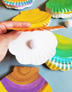 a person holding a plastic toothbrush in front of some colorful seashells on a table