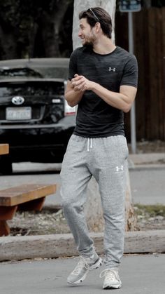 a man in black shirt and grey sweatpants standing on street with his hands together