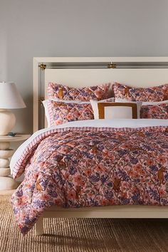 a bed with pink and purple comforter in a bedroom next to two lamps on either side of the bed