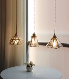 three lights hanging over a white table in front of a mirror and curtained window