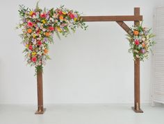 an arch decorated with flowers and greenery in front of a white wall for a wedding ceremony