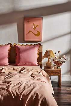 a bed with pink sheets and pillows in a bedroom next to a painting on the wall