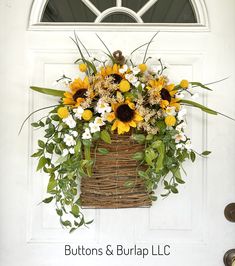 a basket filled with sunflowers and greenery hanging from a white front door