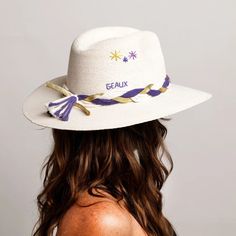 the back of a woman wearing a white hat with purple and gold trimmings