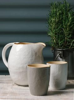 three white vases sitting on top of a wooden table next to a potted plant