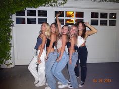 four girls are posing for the camera in front of a garage with their arms up