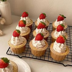 several cupcakes with whipped cream and strawberries on top sit on a cooling rack