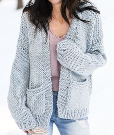 a woman is standing in the snow wearing a gray cardigan sweater and ripped jeans