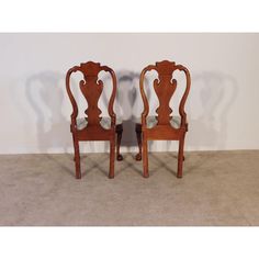 two wooden chairs sitting next to each other on carpeted floor in front of white wall