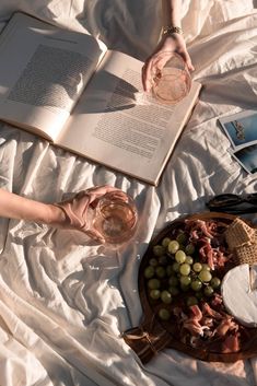 a person laying on a bed with an open book and glass of wine in their hand