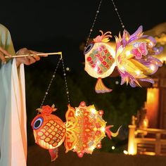 two colorful fish hanging from strings in front of a building with lights on it's sides