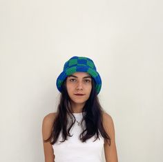 a woman wearing a blue and green knitted hat standing in front of a white wall